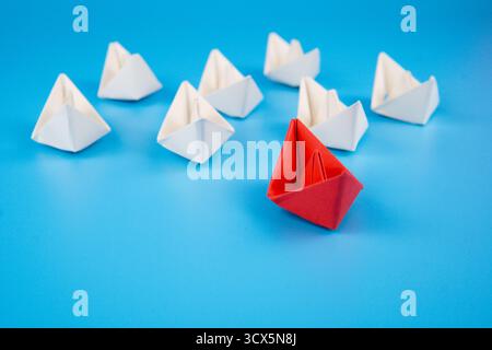 Bateau de papier rouge leader des bateaux de papier blanc sur fond bleu, symbolisant le leadership, l'individualité, le travail d'équipe, la créativité, succès et innovation conc Banque D'Images