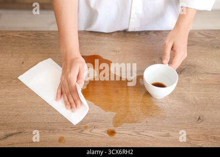 Femme essuyant le café renversé avec une serviette en papier sur la table dans la cuisine, gros plan Banque D'Images