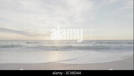 Vagues de l'océan roulant s'approchant du littoral sablonneux lisse au coucher du soleil, sous des nuages pastel éparpillés Banque D'Images