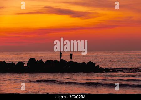 Deux pêcheurs locaux jettent leurs lignes le long de Playa Linda à Ixtapa, au Mexique, lors d’un chaud coucher de soleil tropical sur la côte Pacifique. Banque D'Images