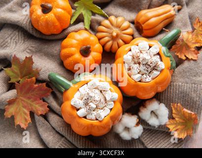 Deux mugs chauffants en forme de citrouille remplis de cacao et de guimauves sur un pull confortable avec un décor d'automne Banque D'Images