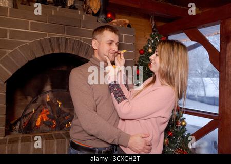 Un homme et une femme se serrent devant une cheminée. La femme porte un pull rose Banque D'Images