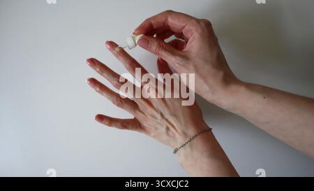 Femme appliquant de l'huile de cuticule à ses ongles. Soin des ongles, routine beauté, concept de soin de la peau. Processus de manucure à domicile. Gros plan des mains avec des ongles roses naturels, une peau saine. Mains de femme caucasienne. Banque D'Images