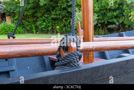 Gros plan d'une corde noire attachée autour d'un poteau en bois sur un bateau. Banque D'Images