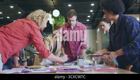 Collaboration six collègues penchés sur une table de conférence avec des tableaux colorés dans un bureau ouvert Banque D'Images