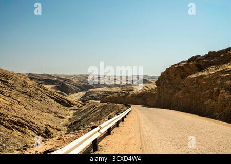 Une route panoramique traversant le parc national Namib-Naukluft en Namibie, entourée de vastes paysages désertiques, de dunes et de montagnes sous un bleu clair Banque D'Images