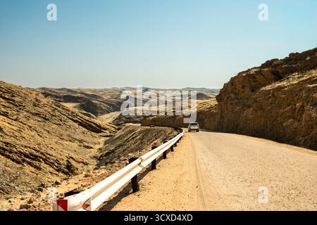 Une route panoramique traversant le parc national Namib-Naukluft en Namibie, entourée de vastes paysages désertiques, de dunes et de montagnes sous un bleu clair Banque D'Images