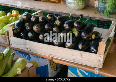 Une caisse en bois rustique remplie d'aubergines violettes fraîches exposées dans un marché de rue en plein air animé, symbolisant les produits naturels et la fraîcheur de la ferme Banque D'Images