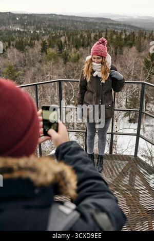 Crop homme avec smartphone prenant la photo de jolie femme debout sur le point élevé dans la vallée des montagnes voyageant ensemble Banque D'Images