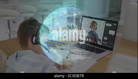 Écriture garçon portant casque à l'aide d'un ordinateur portable à la table à manger avec projection de globe numérique, espace de copie Banque D'Images