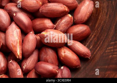 Gros plan d'arachides grillées écaillées en peau rouge sur texture bois Banque D'Images
