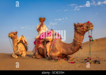 Ancien éleveur de chameaux se reposant avec des chameaux dans le désert du Thar, Rajasthan, Inde Banque D'Images