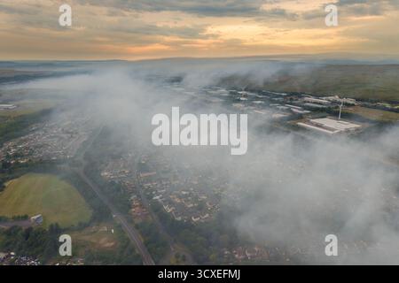 Un ciel spectaculaire au coucher du soleil sur une ville galloise tandis que la fumée d'un feu de forêt couvre la région Banque D'Images