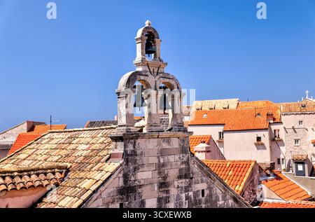Une vue rapprochée du clocher en pierre et des cloches d'une église historique de Dubrovnik, Croatie, se distinguant par un ciel bleu lumineux d'été. Banque D'Images
