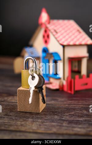 Cadenas et clés placés sur un bloc de bois devant une maison miniature floue, représentant la propriété, la sécurité financière, l'investissement immobilier. Banque D'Images