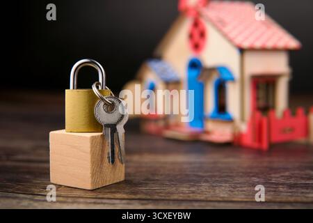 Cadenas et clés placés sur un bloc de bois devant une maison miniature floue, représentant la propriété, la sécurité financière, l'investissement immobilier. Banque D'Images