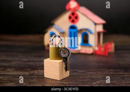 Cadenas et clés placés sur un bloc de bois devant une maison miniature floue, représentant la propriété, la sécurité financière, l'investissement immobilier. Banque D'Images