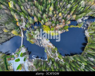 Vue par drone d'une longue étendue d'eau sombre reliant par des rapides, flanquée de passerelles en bois et d'une forêt dense montrant des changements de couleur saisonniers Banque D'Images