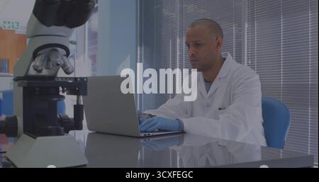 Dactylographie scientifique portant une blouse de laboratoire et des gants saisissant des données sur ordinateur portable dans le laboratoire, avec microscope Banque D'Images