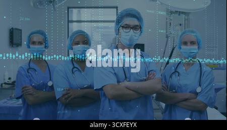 Posant l'équipe médicale portant des gommages bleus sous des lumières chirurgicales dans la salle d'opération, avec stéthoscopes Banque D'Images