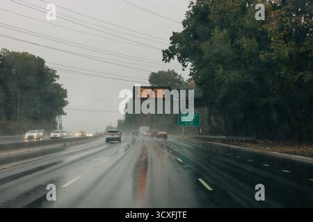 Les véhicules naviguent sur une autoroute mouillée tandis qu'un panneau d'avertissement avertit les conducteurs des conditions de conduite difficiles à venir. Banque D'Images