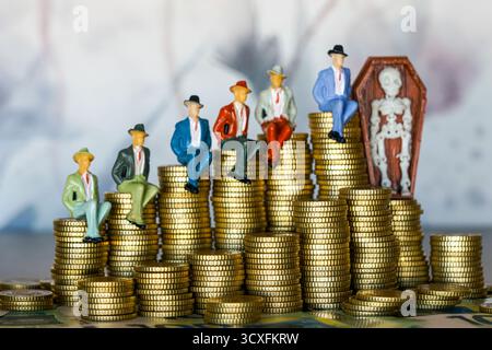Figurines miniatures d'hommes d'affaires assis sur des piles de pièces de monnaie à côté d'un squelette dans le cercueil, symbolisant l'avidité, la richesse, la mortalité, le capitalisme, et conséquences Banque D'Images