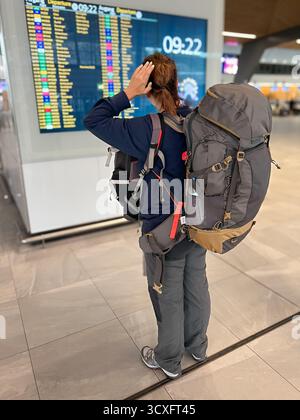 Une jeune femme Backpacker avec un grand sac de voyage regarde le panneau de départ dans un hall d'aéroport, représentant l'aventure, la liberté et l'excitation Banque D'Images