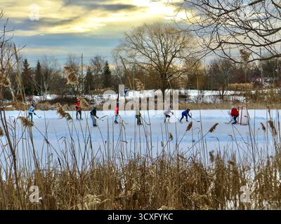 Un groupe d'enfants jouant au hockey sur un étang gelé au milieu d'un parc. Banque D'Images