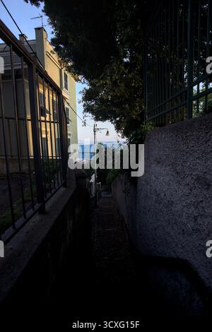 Escalier dans un passage étroit entre bâtiments et murs sur une falaise au coucher du soleil avec une section d'une usine en arrière-plan Banque D'Images