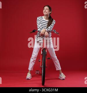 Femme souriante posant sur le vélo sur fond rouge Banque D'Images