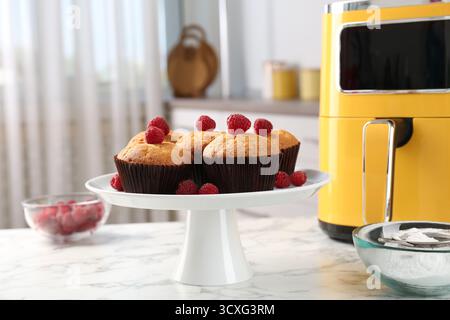 Muffins fraîchement cuits avec framboises et friteuse à air sur table en marbre blanc dans la cuisine Banque D'Images