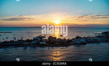 Isla Mujeres, Cancun, Mexique - le soleil se couche sur l'océan, projetant une lueur chaude sur l'eau et les bâtiments sur le rivage Banque D'Images