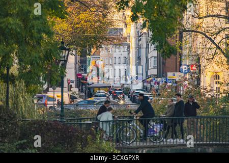 Une scène de rue urbaine animée, capturée à travers la verdure, montre les piétons, les cyclistes et la circulation animée sous la lumière chaude du soir Banque D'Images