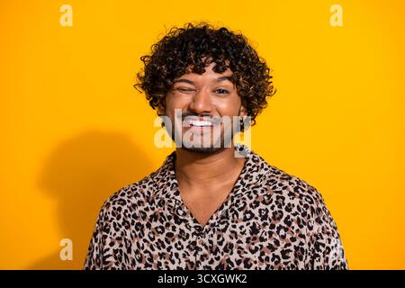 Jeune homme en chemise imprimée léopard pose sur fond jaune avec un sourire joyeux mettant en valeur un look de mode élégant Banque D'Images