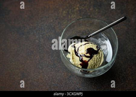 cuillère à crème glacée à la pistache avec sauce au chocolat dans un bol en verre sur fond de table brun foncé, vue de dessus Banque D'Images