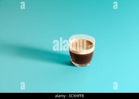 Verre d'espresso frais avec mousse de crème dorée, isolé sur fond turquoise éclatant, composition minimaliste et contrastée Banque D'Images