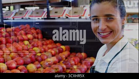 Travailleur souriant portant un tablier rayé, disposant des pommes rouges sur des bacs en bois dans l'allée des fruits et légumes, espace de copie Banque D'Images