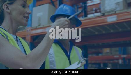 Superviseur et travailleur inspectant les boîtes sur les étagères dans l'entrepôt, avec presse-papiers, gilets et casques de sécurité Banque D'Images