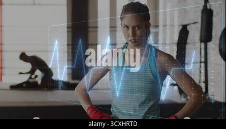 Boxeur femme debout dans un réservoir sarcelle avec des gants rouges dans une salle de boxe, avec superposition de la courbe ECG Banque D'Images