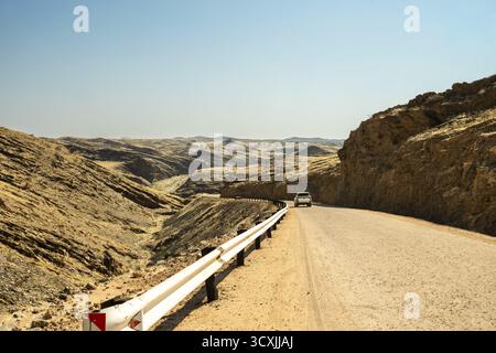 Une route panoramique traversant le parc national Namib-Naukluft en Namibie, entourée de vastes paysages désertiques, de dunes et de montagnes sous un bleu clair Banque D'Images