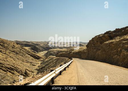 Une route panoramique traversant le parc national Namib-Naukluft en Namibie, entourée de vastes paysages désertiques, de dunes et de montagnes sous un bleu clair Banque D'Images