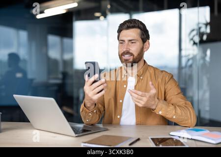 Homme d'affaires ayant une vidéoconférence sur smartphone avec des clients ou des collègues, gestuelle et discutant des détails du projet, montrant la communication moderne Banque D'Images