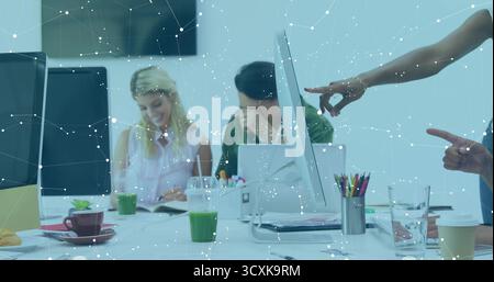 Collaboration collègues examinant des documents autour de la table dans le bureau avec des moniteurs et du jus vert Banque D'Images