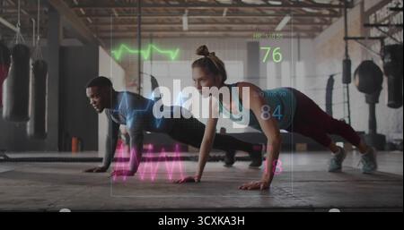 Exécution synchronisée pompes partenaires d'entraînement dans la salle de gym avec sacs de frappe et signes vitaux holographiques Banque D'Images