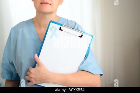 Infirmière féminine ou médecin en uniforme médical tenant une presse-papiers avec un ruban bleu. Sensibilisation au cancer de la prostate en novembre. Bilan de santé, diagnostic, traitement et concept de prévention. Banque D'Images