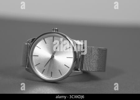Une montre argentée avec un visage noir se trouve sur une surface grise. La montre est réglée sur 10 h 10 Banque D'Images