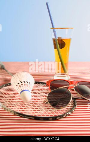 Une raquette de tennis, une paire de lunettes de soleil et un verre de bière sont assis sur une table. La scène transmet une atmosphère détendue et tranquille, comme la personne agréable Banque D'Images