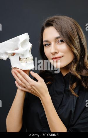 Jeune femme attirante médecin tenant un modèle de squelette de crâne humain dans les mains. Banque D'Images