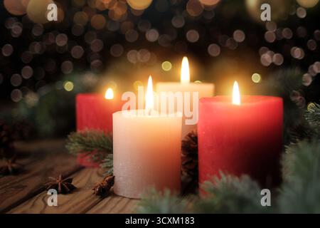 Quatre bougies allumées avec un fond flou foncé. Ambiance de Noël tranquille avec des bougies de l'Avent, des branches de sapin et des lumières Banque D'Images