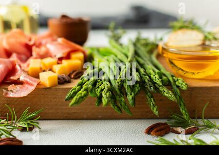 Un tableau de charcuterie dynamique est mis en place pour un rassemblement, mettant en vedette des asperges fraîches, assortiment de fromages, charcuteries et noix. Cette configuration invite les clients à déguster de savoureux bouchées ensemble Banque D'Images